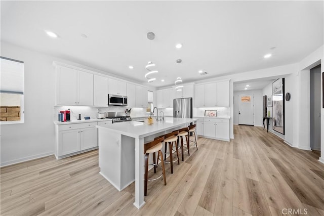 kitchen with a breakfast bar, a center island with sink, stainless steel appliances, light countertops, and white cabinets