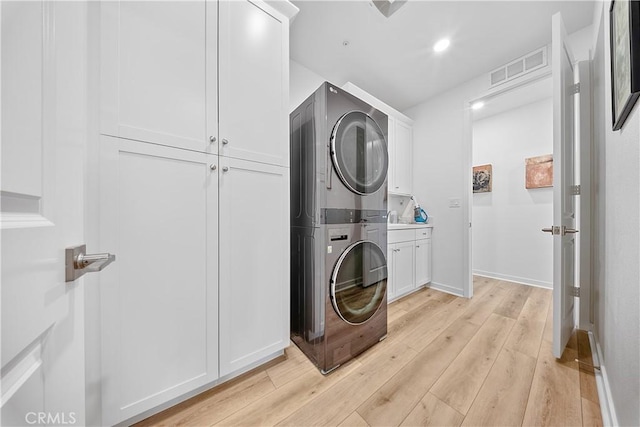 clothes washing area featuring stacked washer and dryer, visible vents, baseboards, light wood-type flooring, and cabinet space