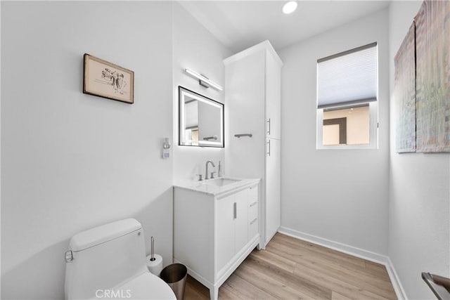 bathroom featuring baseboards, toilet, wood finished floors, vanity, and recessed lighting