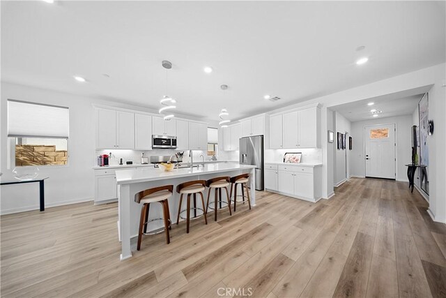 kitchen featuring pendant lighting, white cabinetry, stainless steel appliances, light hardwood / wood-style floors, and a center island with sink