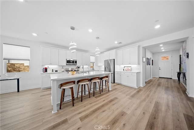 kitchen with a breakfast bar area, stainless steel appliances, white cabinets, light countertops, and a center island with sink