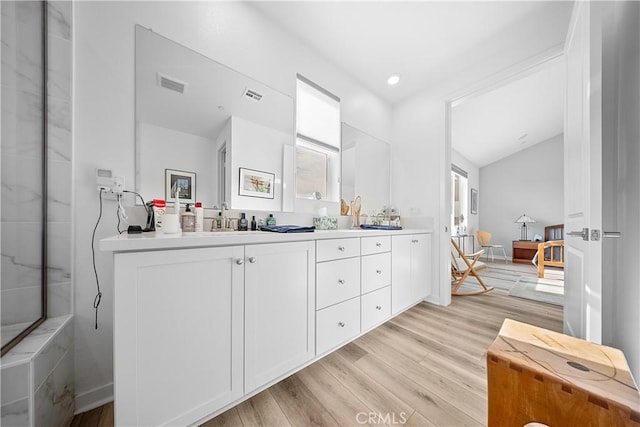 full bathroom with lofted ceiling, wood finished floors, a sink, visible vents, and double vanity