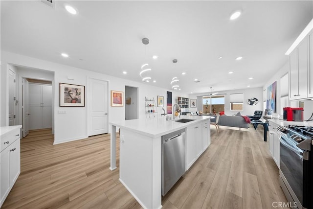 kitchen featuring decorative light fixtures, stainless steel appliances, an island with sink, and white cabinets