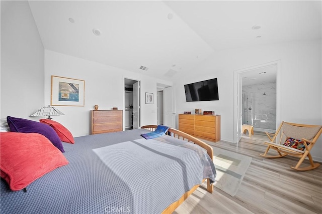 bedroom featuring lofted ceiling, connected bathroom, and light hardwood / wood-style flooring