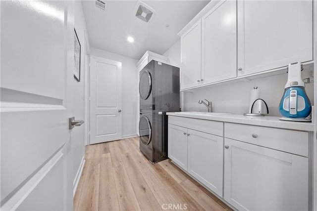 clothes washing area with cabinets, stacked washer / dryer, light hardwood / wood-style floors, and sink