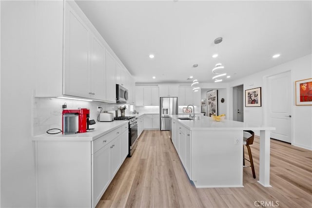 kitchen featuring sink, appliances with stainless steel finishes, a kitchen island with sink, white cabinetry, and hanging light fixtures