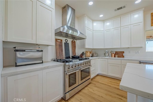 kitchen with white cabinetry, light stone countertops, wall chimney range hood, light hardwood / wood-style floors, and double oven range