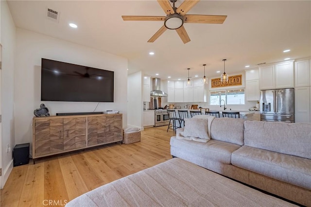 living room featuring ceiling fan, sink, and light hardwood / wood-style flooring