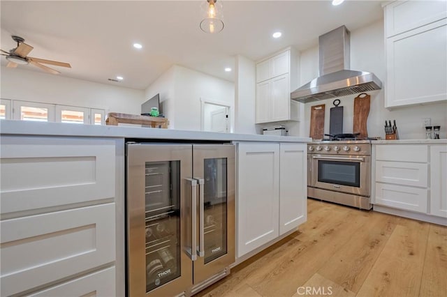 kitchen featuring high end range, white cabinets, light wood-type flooring, wall chimney exhaust hood, and wine cooler