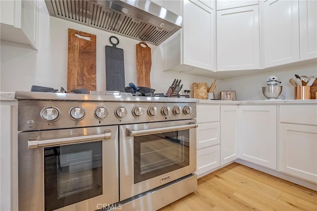 kitchen featuring double oven range, white cabinetry, wall chimney range hood, and light wood-type flooring