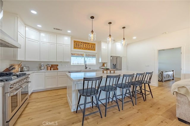 kitchen featuring pendant lighting, white cabinets, wall chimney exhaust hood, a kitchen island, and high end appliances