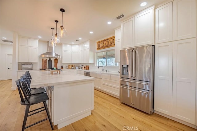 kitchen featuring white cabinets, light stone countertops, a center island, wall chimney range hood, and stainless steel appliances