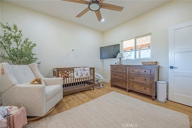 bedroom with ceiling fan, a nursery area, and hardwood / wood-style flooring