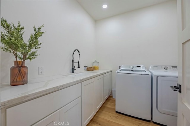 laundry room with sink, washer and clothes dryer, light hardwood / wood-style floors, and cabinets