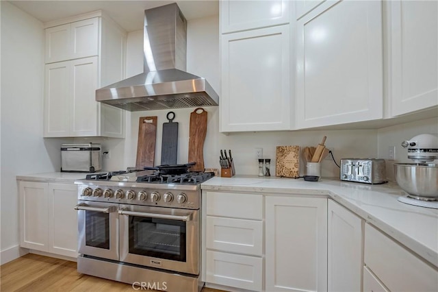 kitchen featuring white cabinetry, double oven range, wall chimney range hood, and light hardwood / wood-style floors