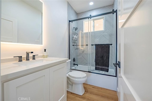 full bathroom featuring wood-type flooring, enclosed tub / shower combo, vanity, and toilet