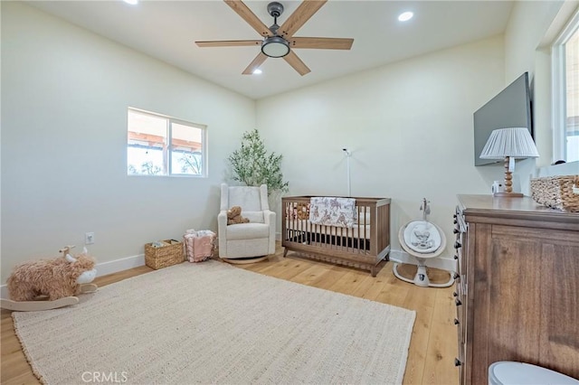 bedroom with ceiling fan, wood-type flooring, and a nursery area