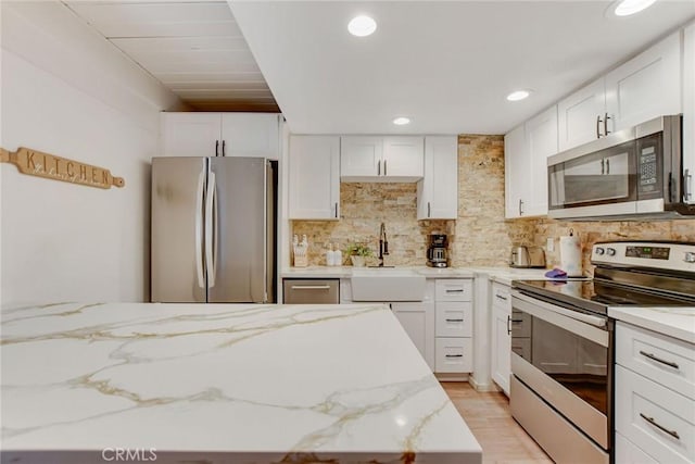 kitchen featuring sink, light stone counters, white cabinetry, and appliances with stainless steel finishes