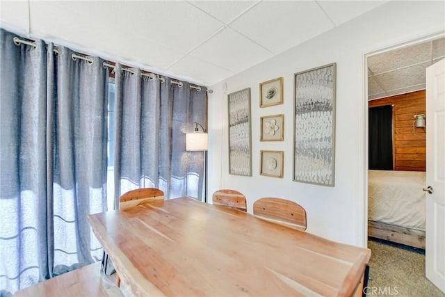 dining space with a paneled ceiling, wooden walls, and carpet