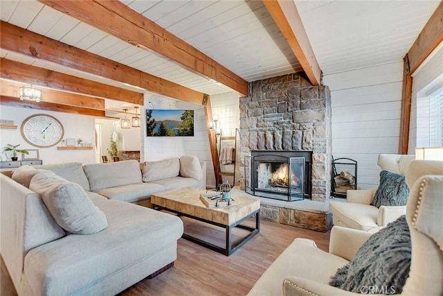 living room with light hardwood / wood-style flooring, beam ceiling, and a stone fireplace