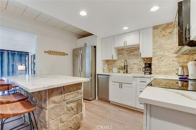 kitchen featuring decorative backsplash, white cabinets, sink, a breakfast bar, and stainless steel appliances