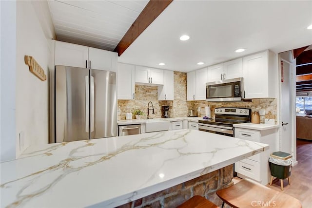 kitchen with light stone counters, white cabinets, appliances with stainless steel finishes, and sink