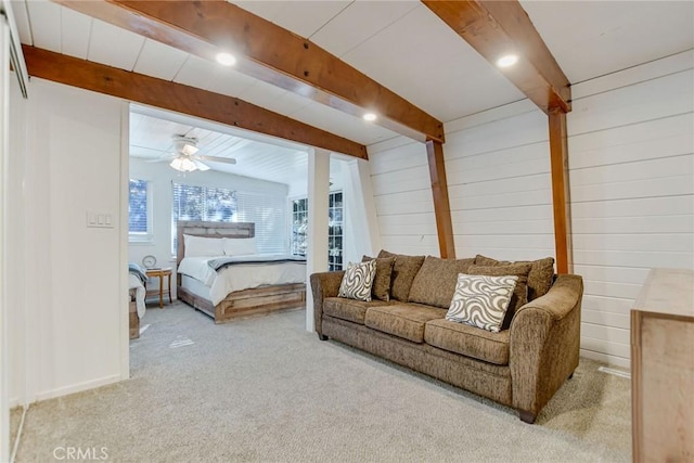 bedroom featuring wood walls, light colored carpet, beamed ceiling, and ceiling fan