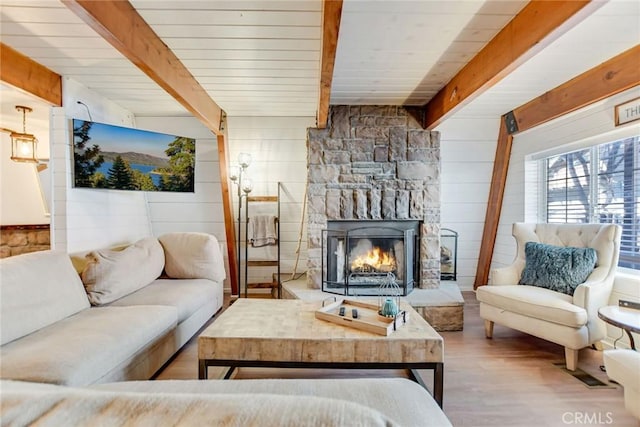 living room featuring beamed ceiling, hardwood / wood-style floors, and a stone fireplace