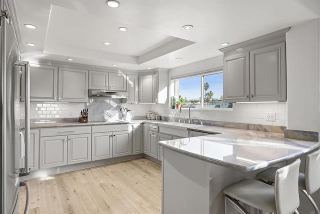 kitchen featuring light hardwood / wood-style flooring, sink, kitchen peninsula, a raised ceiling, and gray cabinetry