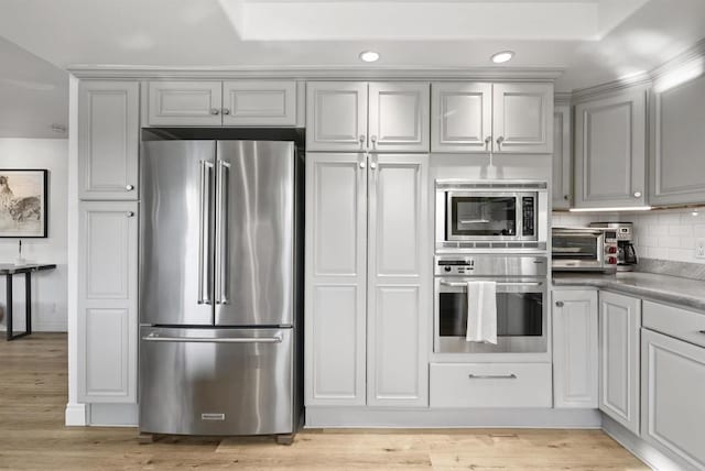 kitchen featuring light hardwood / wood-style floors, backsplash, appliances with stainless steel finishes, and gray cabinetry