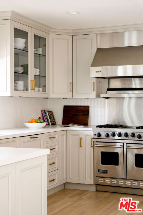 kitchen featuring wall chimney exhaust hood, backsplash, light wood-type flooring, white cabinets, and double oven range