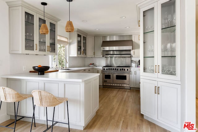 kitchen featuring wall chimney range hood, double oven range, sink, hanging light fixtures, and kitchen peninsula