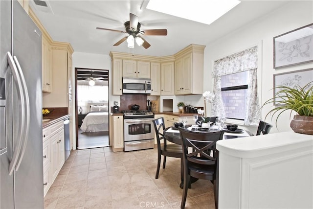 kitchen with dark countertops, cream cabinets, appliances with stainless steel finishes, and ceiling fan