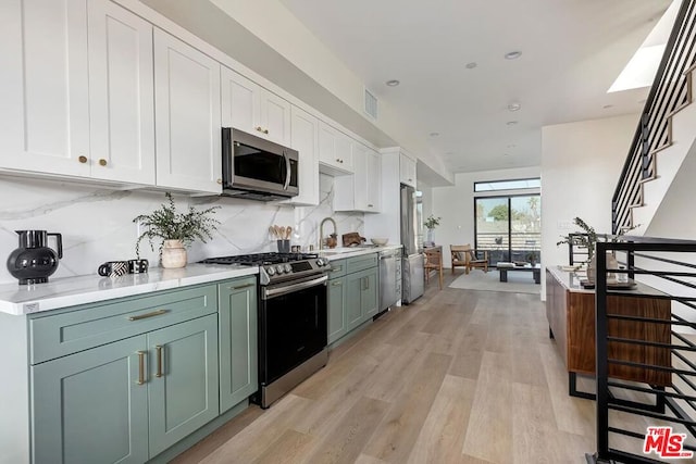 kitchen with white cabinetry, stainless steel appliances, tasteful backsplash, light hardwood / wood-style floors, and sink