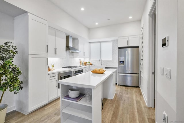 kitchen featuring white cabinetry, wall chimney range hood, a kitchen island, sink, and stainless steel appliances