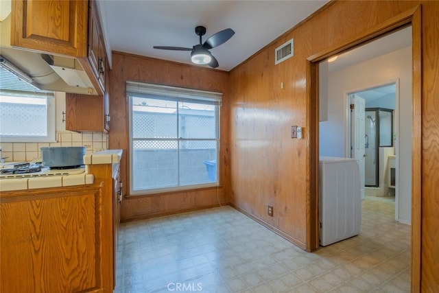 kitchen featuring ceiling fan, washer / dryer, tile countertops, wood walls, and decorative backsplash