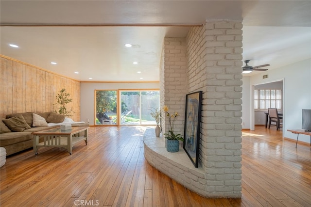 living room featuring light hardwood / wood-style floors, wooden walls, ceiling fan, and a fireplace