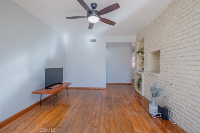 unfurnished living room featuring hardwood / wood-style flooring, brick wall, built in shelves, and ceiling fan