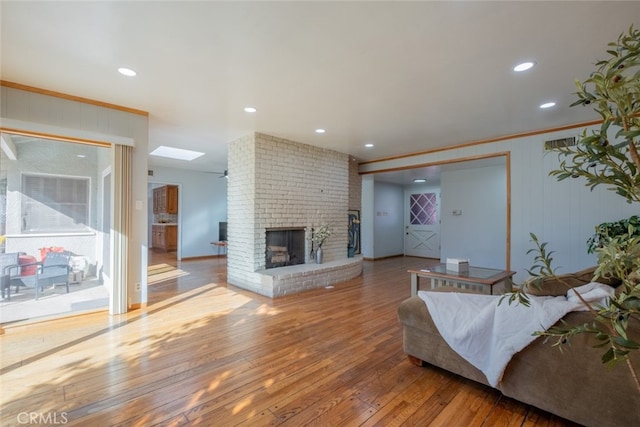 living room featuring a brick fireplace, hardwood / wood-style floors, crown molding, and a skylight