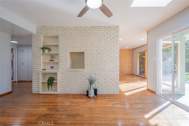 unfurnished living room featuring built in shelves, hardwood / wood-style flooring, a skylight, and ceiling fan