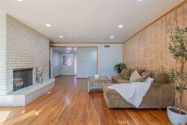 living room with a fireplace, wood walls, light hardwood / wood-style floors, and crown molding