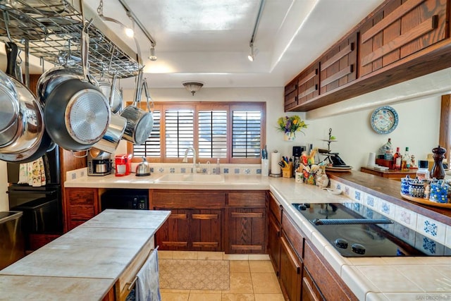 kitchen with sink, rail lighting, black electric stovetop, tile counters, and light tile patterned flooring