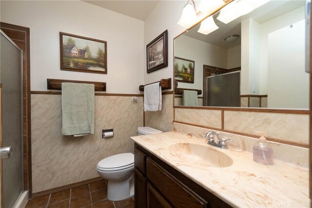 bathroom featuring tile patterned flooring, tile walls, toilet, a shower with shower door, and vanity