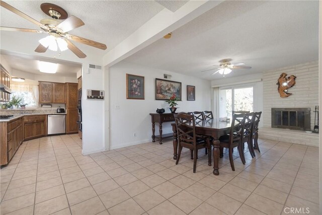 tiled dining room with a brick fireplace, plenty of natural light, a textured ceiling, and ceiling fan