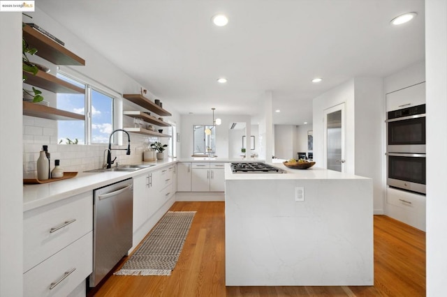 kitchen featuring pendant lighting, appliances with stainless steel finishes, white cabinetry, light hardwood / wood-style floors, and sink