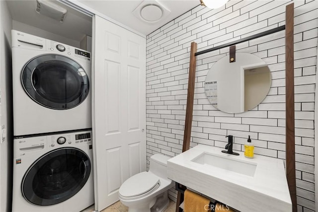 bathroom with sink, toilet, stacked washer and clothes dryer, and tile walls