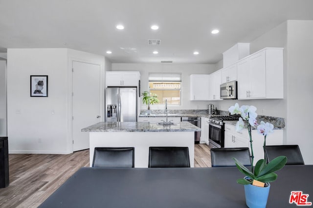 kitchen with white cabinetry, stainless steel appliances, a center island, and light hardwood / wood-style floors