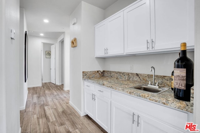 kitchen with sink, light stone counters, white cabinets, and light hardwood / wood-style floors