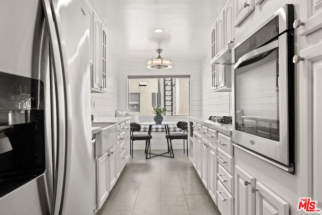 kitchen featuring wood walls, white cabinetry, hanging light fixtures, and stainless steel appliances