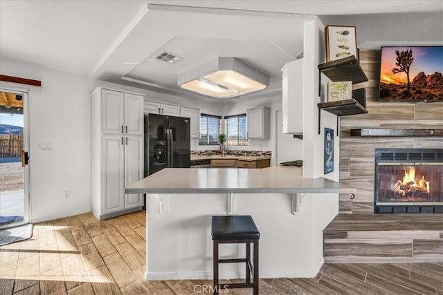 kitchen with white cabinets, a kitchen bar, black refrigerator with ice dispenser, kitchen peninsula, and a tiled fireplace